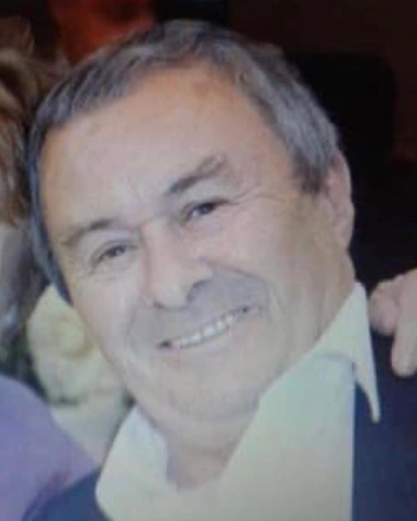 A smiling older man with short grey hair, wearing a dark suit and white shirt.