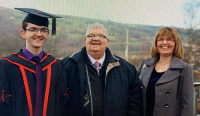 Three people pose together outdoors, with mountains in the background, celebrating a graduation.