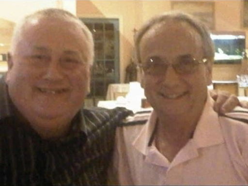 Two smiling men posing together in a casual dining setting.