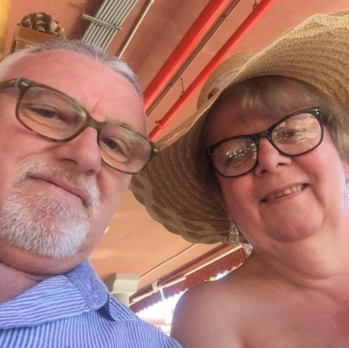 Two smiling adults, one wearing glasses and a wide-brimmed hat, sitting together.