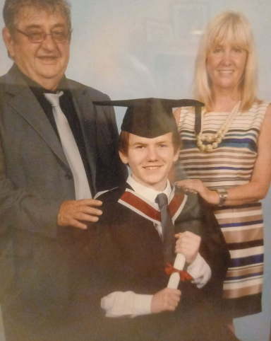A young man in graduation attire poses with two adults, smiling proudly.