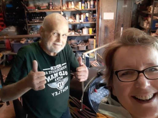 A cheerful older man giving thumbs up alongside a smiling woman in a workshop setting.