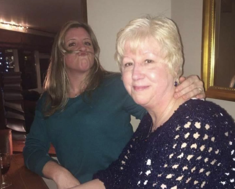 Two women smiling together, one with long hair and the other with short, light-coloured hair.