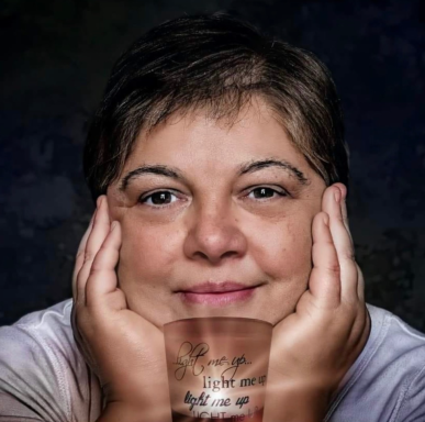 Woman smiling with hands on her cheeks, featuring visible tattoos on her forearms.