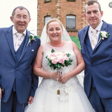 Bride in a white dress holding flowers, with two men in blue suits beside her.