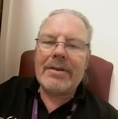 Man with glasses and a beard smiling while sitting in a chair.