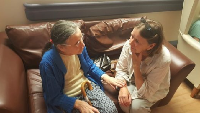Two women engaged in a heartfelt conversation, sitting on a sofa in a cozy setting.