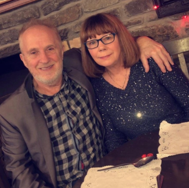 A smiling couple posing together at a table with a decorative tablecloth.