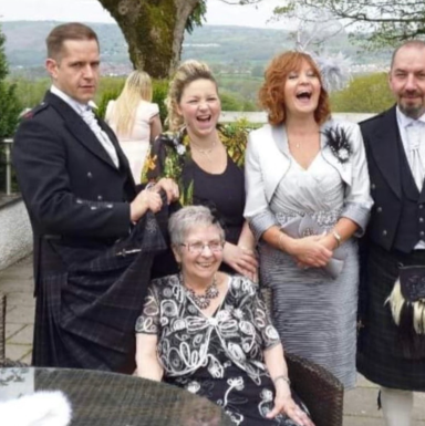 A group of five people, smiling and dressed formal, posing outdoors.