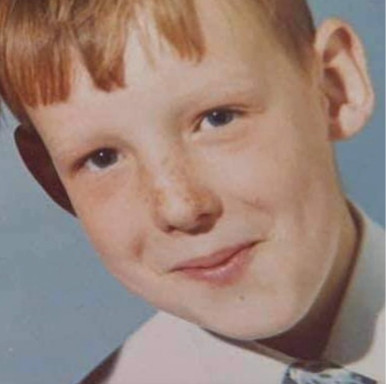 A smiling boy with light brown hair and freckles, wearing a collared shirt and tie.