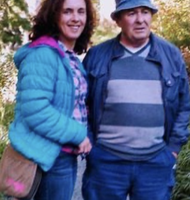 A woman in a blue jacket and a man in a hat stand together outdoors.