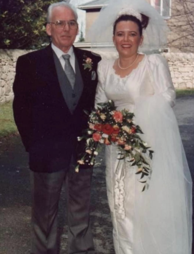 Bride in a wedding dress holding a bouquet, standing with a man in a grey suit.