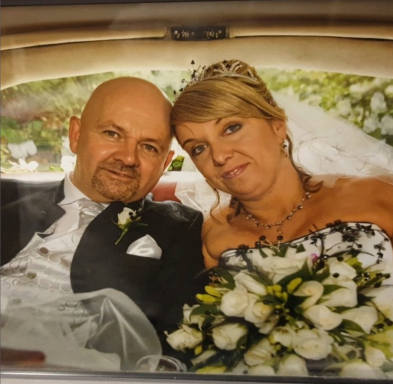 A smiling couple in formal attire, sitting together with a bouquet, in a car.