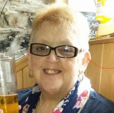 Smiling woman with glasses holding a drink, wearing a blue top and patterned scarf.