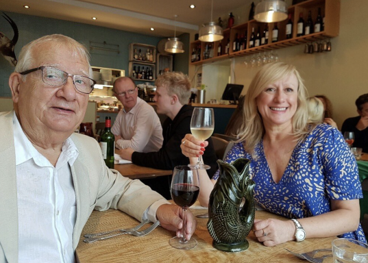 A man and a woman smiling, holding drinks in a restaurant setting.
