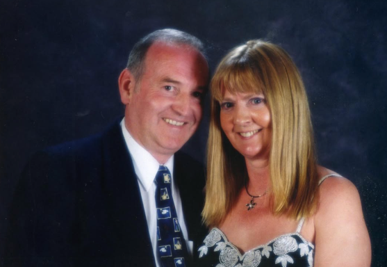 A smiling couple, casually dressed, posed together against a dark background.