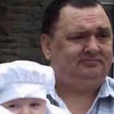 A man stands beside a baby wearing a white chef's hat.
