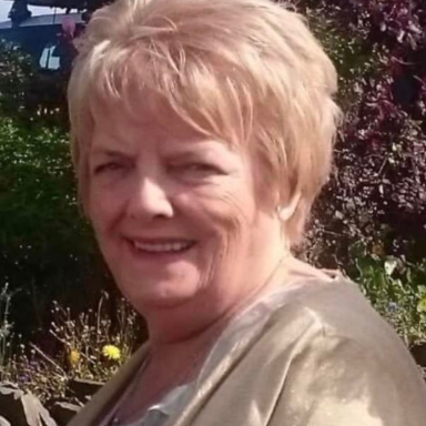 A smiling woman with short blonde hair, wearing a light-coloured top, in a garden setting.