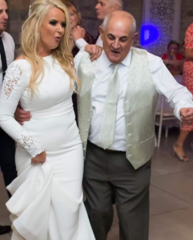 A woman in a white dress dancing with an older man in a vest at a celebration.