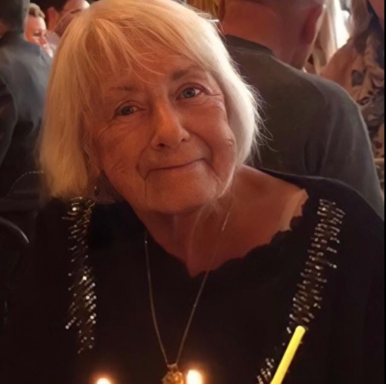 Older woman with short blonde hair, smiling, celebrating with birthday candles.